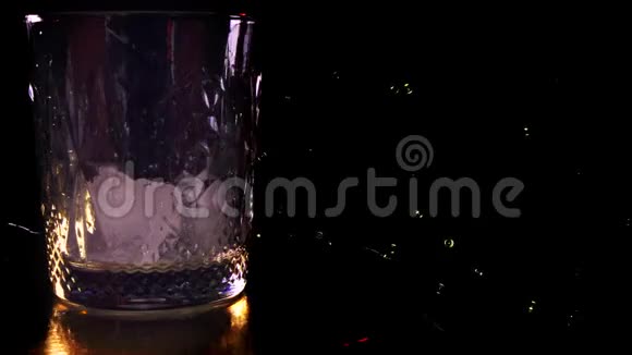 特写镜头威士忌酒杯的侧面VIEW将苏格兰威士忌或白兰地倒入装有冰块的玻璃杯中放在深色视频的预览图