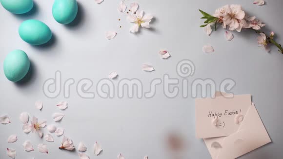 带着复活节彩蛋和贺卡的花瓣落在蓝色背景上视频的预览图