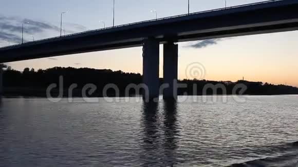 日落的景色来自一艘游船在河波上摇摆在一座有着燃烧的灯光的桥下航行特写镜头视频的预览图