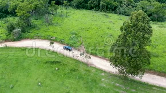 在绿色热带山谷中央的一条小土路上驾驶汽车的鸟瞰图视频的预览图