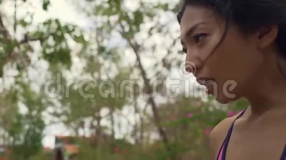 慢动作万向节拍摄年轻迷人疲惫口渴的亚洲女性在艰苦的跑步锻炼后饮水降温视频的预览图