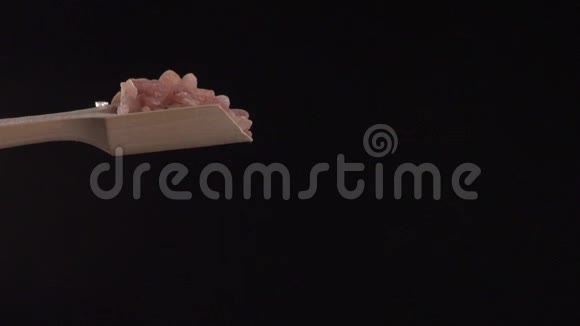 在黑色背景下粉色喜马拉雅盐从一个木勺上往下缓慢地加入视频的预览图