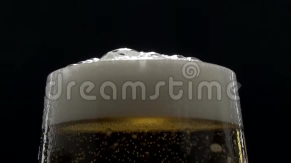 黑色背景下的啤酒杯中冒出细泡一杯啤酒的特写镜头慢动作的泡沫视频的预览图