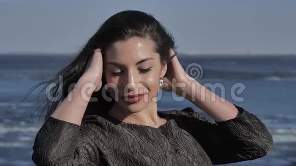 一个穿着黑色裙子的小女孩在阳光明媚的大海中抚摸着她的头发视频的预览图
