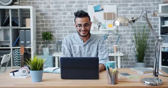 阿拉伯上班族使用笔记本电脑在工作场所的办公桌上微笑的慢动作视频的预览图