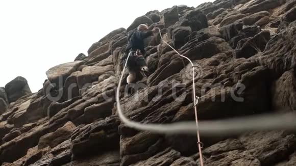一个雄性登山者在雨中保护一条爬岩石路线的绳子视频的预览图
