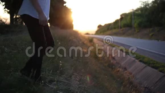 日落时分年轻人坐在草地上从可重复使用的钢制热瓶中喝水靠近沥青路视频的预览图