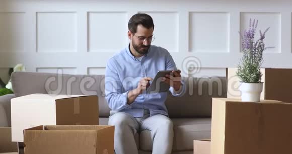 使用数码平板电脑的年轻人坐在沙发上拿着盒子视频的预览图