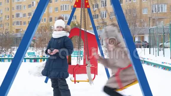 在冬天的城市度假时少女在下雪的操场上摇摆快乐的女朋友荡秋千视频的预览图
