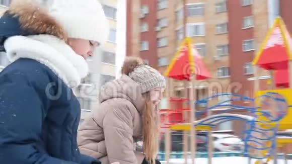 笑的少女在冬天散步时旋转旋转木马在雪地操场上摇摆女朋友的观点视频的预览图