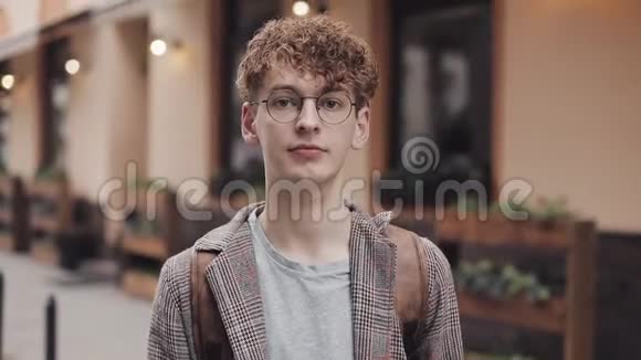 一张年轻人的特写照片他留着红色卷发戴着眼镜身穿t恤和夹克拎着包站在老城视频的预览图