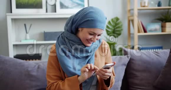 戴着头巾的混血女孩在家用智能手机触摸屏幕视频的预览图