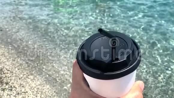 男性手拿一个一次性咖啡杯在海滩背景视频的预览图