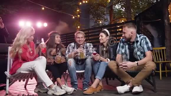 很高兴和朋友在一起四个年轻人在院子里坐在椅子上聊天喝啤酒视频的预览图