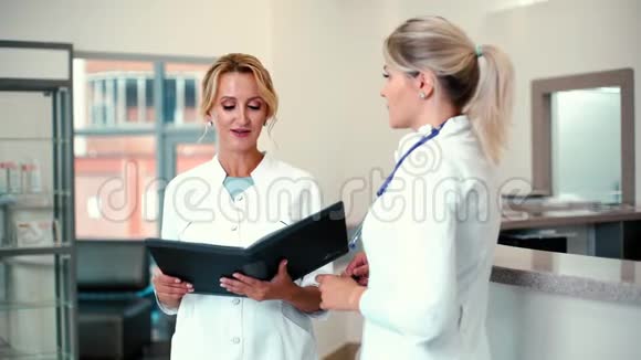 两名女医生站在医院里拿着剪贴板讨论病例视频的预览图
