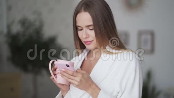 金发女郎的肖像使用电话在厨房端着一杯咖啡或茶视频的预览图