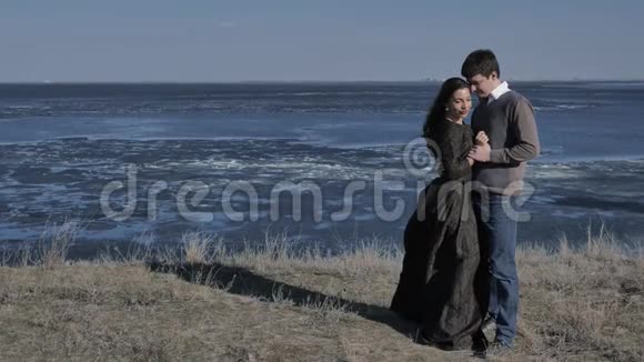 一对年轻夫妇穿着深色的衣服沿着海滨散步阳光明媚的一天视频的预览图