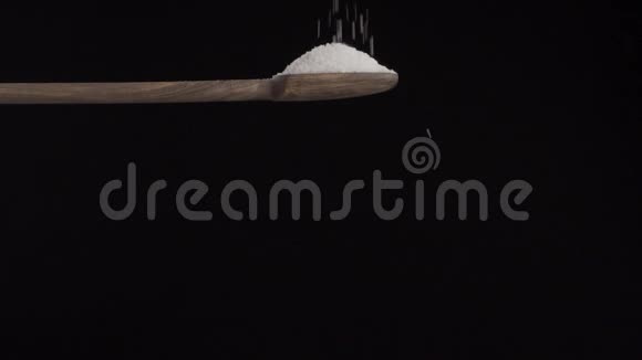 盐从上面倒入一个木勺隔离在黑色的背景上视频的预览图