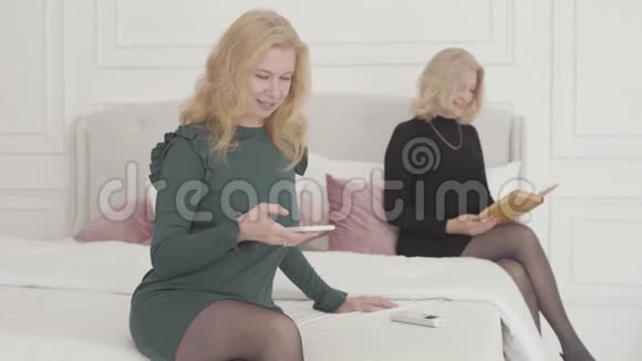 富有的高加索女人穿着优雅的衣服坐在卧室里看书带着微笑的金发女人视频的预览图