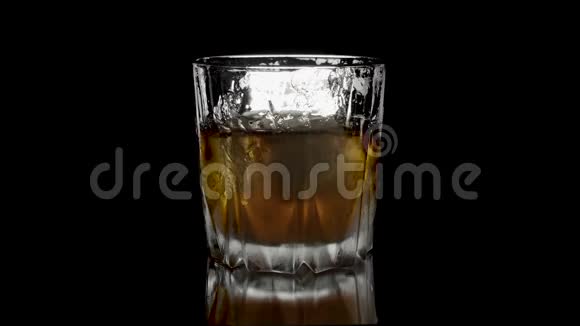 冰块在一杯威士忌中旋转融化孤立在黑色背景上在白色威士忌中旋转冰块视频的预览图