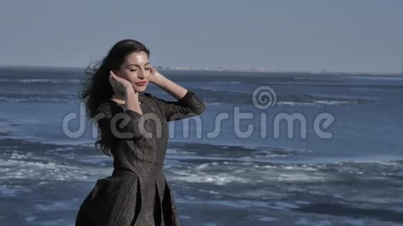 一个穿着黑色裙子的小女孩在阳光明媚的大海中抚摸着她的头发视频的预览图