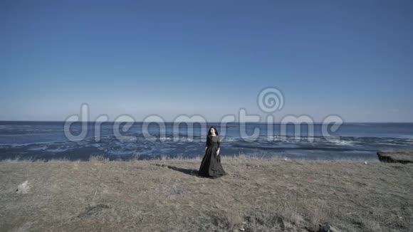 一个穿着黑色衣服的年轻女孩站在岸边在背景海洋里阳光明媚的一天视频的预览图