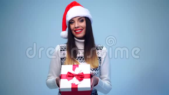 年轻漂亮性感的圣诞女孩穿着白色毛衣戴着可爱的圣诞帽打开一个红色的大礼盒视频的预览图