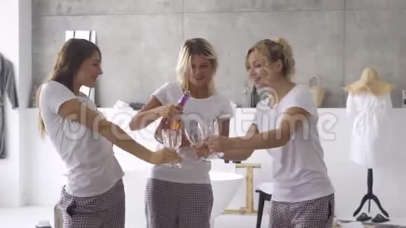 三个快乐的女朋友穿着同一件睡衣一起在家喝酒一位女士倒香槟视频的预览图
