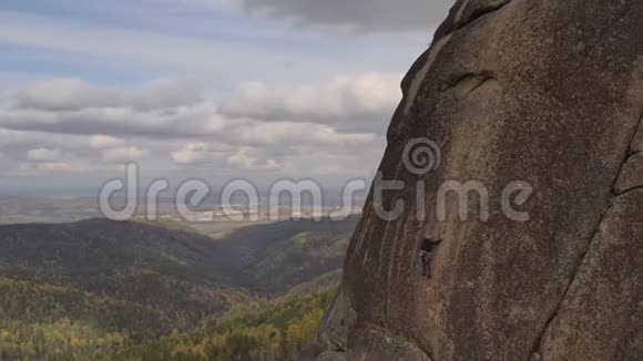 一个年轻人爬上一座垂直墙上的山顶俯瞰着山谷视频的预览图
