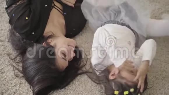 特写镜头一位微笑的中东年轻女子和她可爱的女儿躺在柔软的地毯旁快乐的母亲消费视频的预览图