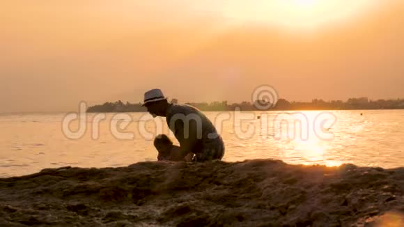 年轻的父亲和他的孩子在海滩日落时玩得很开心父亲在海里和孩子玩耍的剪影父亲视频的预览图