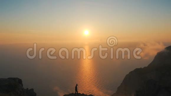 一位年轻女子沿着悬崖边走着从高处看到海面上美丽的戏剧性日落视频的预览图