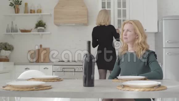 两个漂亮的金发白种人女人坐在豪华的厨房里准备喝酒成熟的富婆视频的预览图