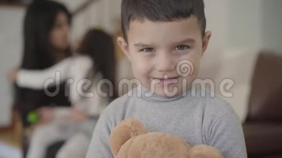 一个迷人的中东灰眼男孩的特写脸黑发男孩拿着泰迪熊看着相机视频的预览图