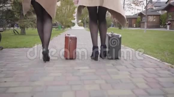 两位身着米色外套戴着头巾和太阳镜的成熟白人女性朋友拿着旧旅行包和视频的预览图