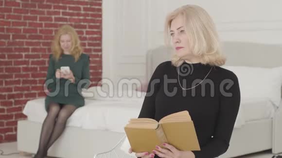 一位美丽的白种人女人坐在书上看着远处的特写肖像带着灰色笑容的成熟女人视频的预览图