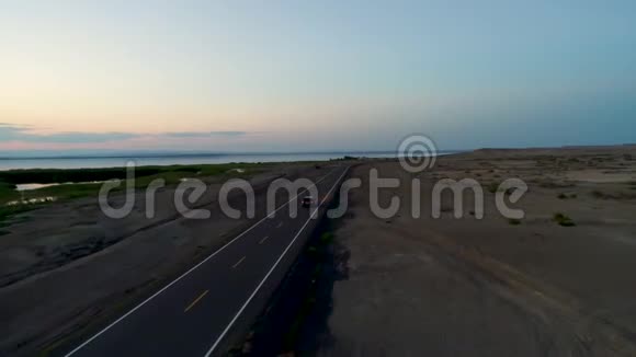 日落时在湖边沙漠的一条空路上驾车的鸟瞰图视频的预览图