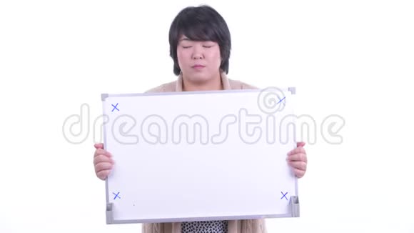 穿着超重的亚洲女人拿着白板在冬天得到坏消息视频的预览图