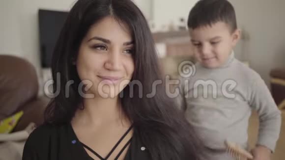 一个中东榛眼女人的肖像被一个微笑的小男孩梳在后台儿子关心视频的预览图