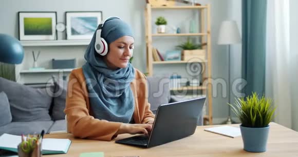 穆斯林女孩在家里用手提电脑和耳机听音乐视频的预览图