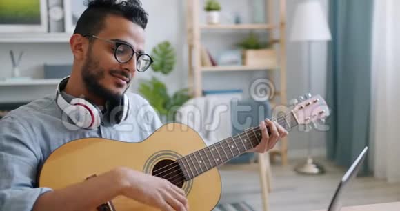 阿拉伯音乐家在家里手提电脑前弹吉他的慢动作视频的预览图