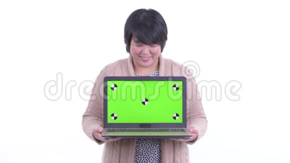 快乐超重的亚洲女人一边思考一边展示准备过冬的笔记本电脑视频的预览图