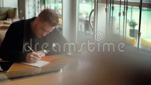 年轻的帅哥正在写蓝图坐在舒适的咖啡馆里的桌子旁视频的预览图