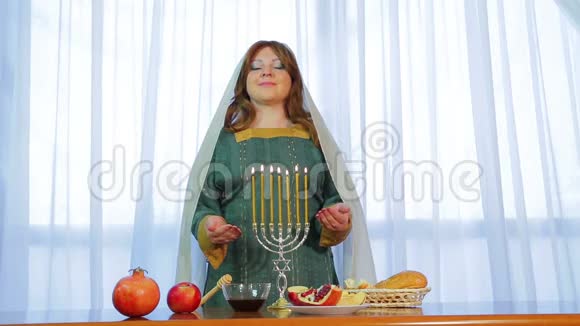 一位犹太妇女站在节日的餐桌前在罗什哈沙纳前夕点燃蜡烛视频的预览图