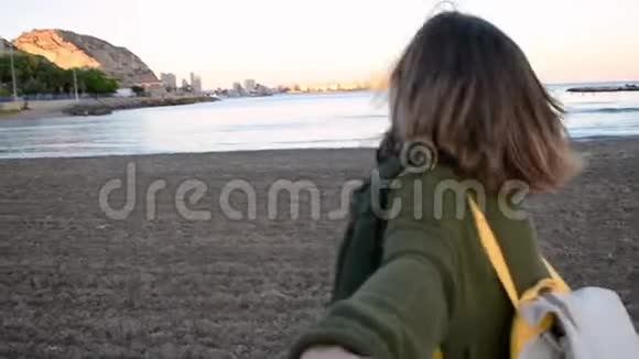 年轻的女人牵着一只男人的手他们在海滩上奔跑慢动作视频的预览图