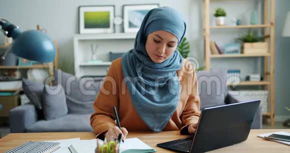 穆斯林女孩自由职业者在家里用笔记本电脑和笔记本电脑工作视频的预览图