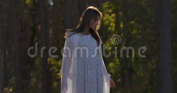 迷人的白种人女孩站在阳光下的森林看着一边穿着浅色白裙的美女视频的预览图