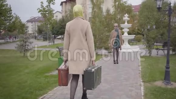 后景白种人女人带着两个旅行袋走到微笑的朋友身边拥抱她两个成熟的人视频的预览图