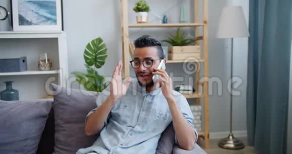 一个英俊的阿拉伯男人在手机上聊天在家里的沙发上笑视频的预览图