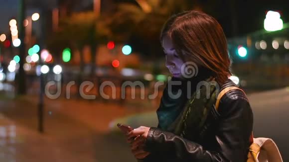 年轻女子晚上在街上看她的智能手机慢动作视频的预览图